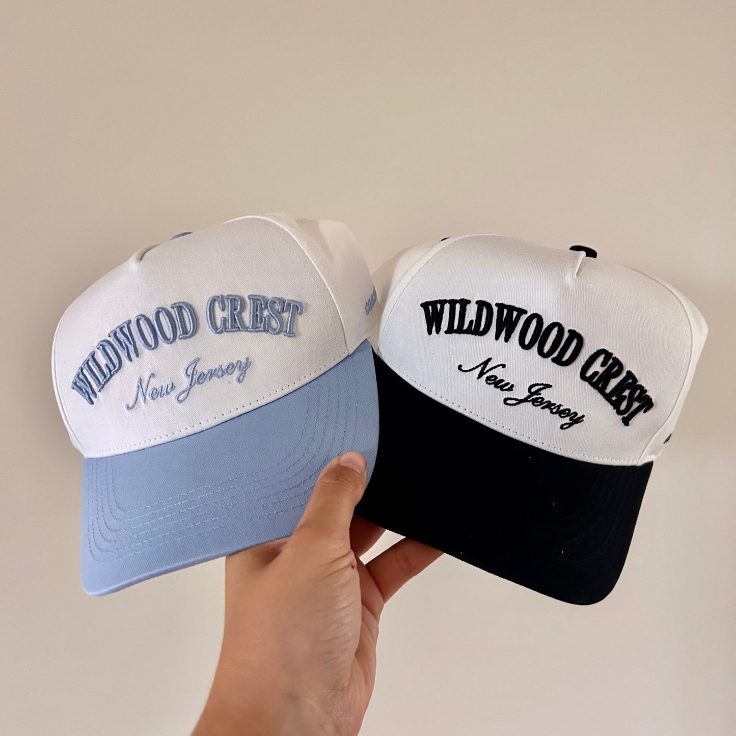 Two baseball caps with 'Wildwood Crest, New Jersey' text held by a hand against a plain background.
