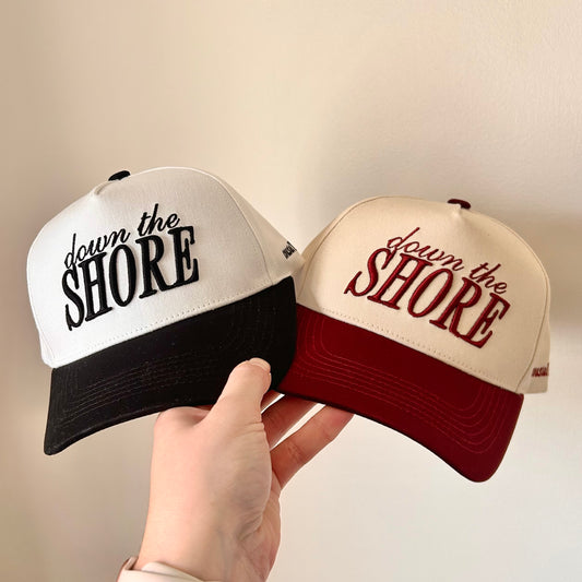 Two baseball caps with 'down the Shore' text held by a hand against a neutral background