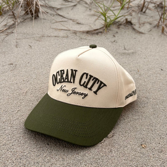 Beige cap with 'Ocean City' text on sandy ground with grass