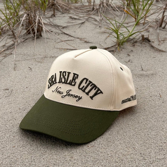 Beige and green hat saying "Sea Isle City New Jersey" on a sandy surface with grass
